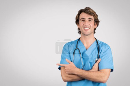 Lächelnde Krankenschwester in blauer Uniform zeigt selbstbewusst zur Seite in den freien Raum und zeigt freundliches Auftreten und Erreichbarkeit in medizinischer Umgebung