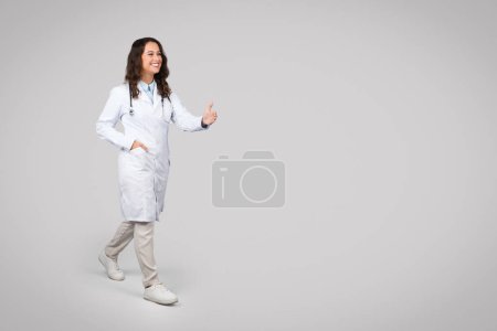 Photo for Positive european woman doctor with stethoscope, in uniform give hand to patient to handshake on light background, full length, free space. Medical services, professional health care - Royalty Free Image