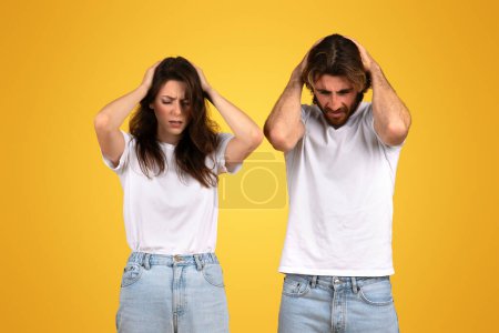 Photo for Distressed european man and woman with hands on their heads, displaying expressions of intense stress or headache, clad in simple white t-shirts against a stark yellow background - Royalty Free Image