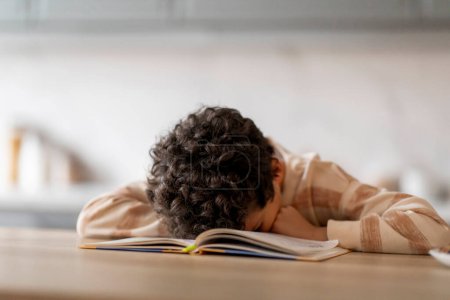 Foto de Niño negro agotado durmiendo en los libros mientras hacía la tarea escolar, niño afroamericano cansado preparándose para el examen, acostado en el escritorio en casa, colocando la cabeza en los libros de trabajo, durmiendo en la mesa, primer plano - Imagen libre de derechos
