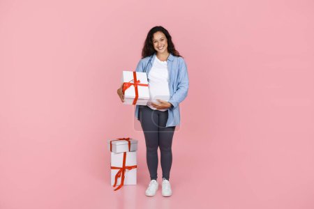 Photo for Happy young pregnant woman have baby shower, holding presents. Expecting lady celebrating expected birth on pink studio background, holding gift boxes, full length, copy space - Royalty Free Image