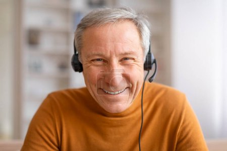Photo for Closeup photo of handsome senior man using headset smiling at camera. Grandfather working from home, attending online meeting with colleagues, have job at call center - Royalty Free Image
