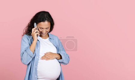 Téléchargez les photos : Femme enceinte souriante parlant sur son smartphone. Heureuse femme enceinte ont agréable parler au téléphone et toucher son ventre, posant sur fond de studio rose, panorama avec espace de copie - en image libre de droit