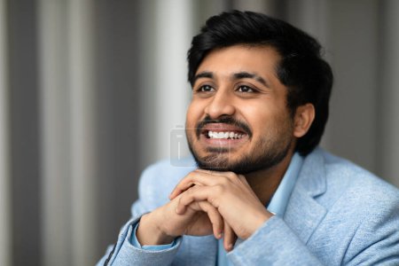 Photo for Portrait of successful smiling Middle Eastern businessman looking aside, exuding confidence and professionalism, poses with his chin on hands in a contemporary office indoors - Royalty Free Image