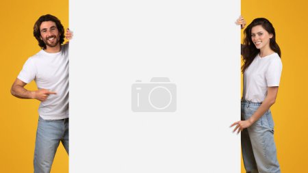 Photo for Cheerful european young couple sharing a fun moment with a smartphone on a bright yellow background, embodying connectivity and joyful interaction in a casual setting, studio - Royalty Free Image