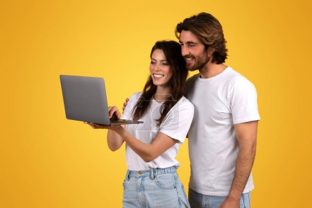 Photo for Enthusiastic european young couple collaboratively using a laptop computer, showing teamwork and a shared digital experience, against an inviting yellow background, studio - Royalty Free Image