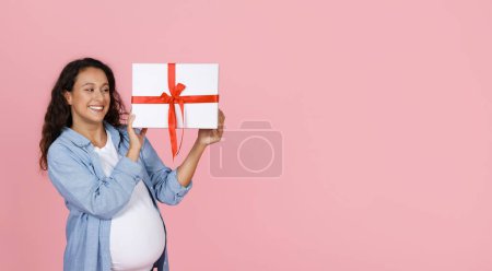 Photo for Excited happy young pregnant woman with big tummy holding white gift box with red bow, have baby shower, panorama with copy space, isolated on pink studio background - Royalty Free Image