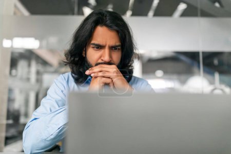 Photo for Concentrated millennial Indian man in formal outfit manager looking for creative solution, sitting at desk at modern office, working on laptop computer, closeup, copy space - Royalty Free Image