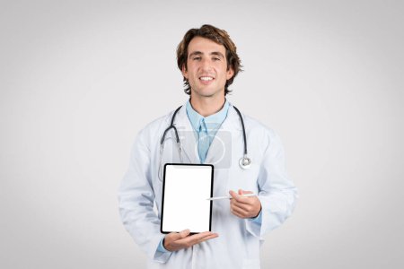 Foto de Médico varón sonriente con estetoscopio alrededor del cuello que presenta una pantalla de tableta vacía adecuada para publicidad de aplicaciones médicas o visualización de información de salud - Imagen libre de derechos