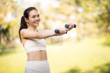 Photo for A radiant glad caucasian young woman athlete exercises with dumbbells outdoors, her smile conveying the joy of a healthy lifestyle in a serene park setting, enjoy workout at city outside - Royalty Free Image