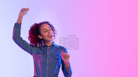 Photo for Radiant black lady with curly hair with closed eyes, dancing in denim shirt, feeling the beat on neon pink and purple gradient background, panorama, free space - Royalty Free Image