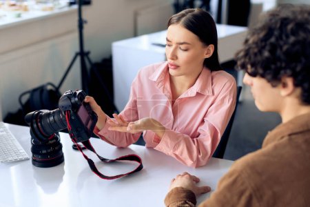 Gestos de fotógrafa femenina mientras discute fotos con el modelo masculino enfocado que lleva una chaqueta marrón, comprometida en un diálogo creativo sobre la pantalla de la cámara