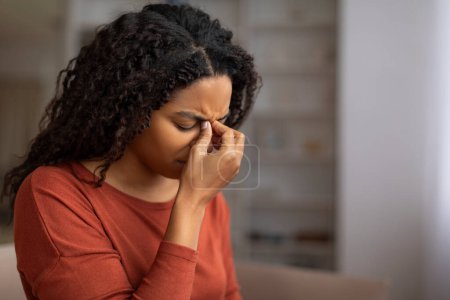Photo for Young black woman feeling sinus pain, pressing on the bridge of her nose, sick african american woman closing eyes and frowning, showing signs of discomfort or headache at home, closeup - Royalty Free Image