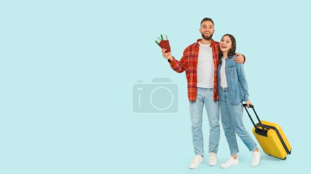 Photo for Happy Young Tourists Couple Ready For Vacation, Standing With Yellow Suitcase, Passports And Travel Tickets Over Blue Background In Studio, Full Length Shot, Panorama With Empty Space - Royalty Free Image
