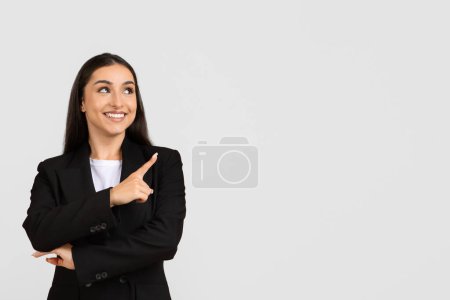 Photo for Cheerful young businesswoman in black suit pointing upwards at free space, indicating new idea or business concept on grey background, banner - Royalty Free Image