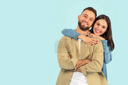 Photo for Happy European Young Couple Hugging While Posing Over Blue Studio Backdrop, Standing Near Copy Space For Advertisement Text, Smiling To Camera. Portrait Of Wife Hugging Husband From Back - Royalty Free Image