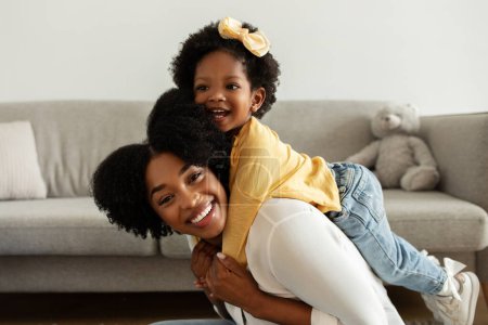 Photo for Family, affection. Happy young black mother lifting up her pretty little daughter, joyful african american mom and kid baby girl having fun together at home, looking at camera and smiling, copy space - Royalty Free Image