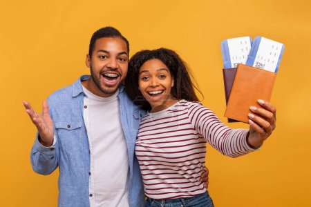 Joyful young black couple holding passports and boarding passes, happy african american man and woman excited for their upcoming travel, standing against vibrant yellow background, closeup
