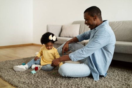 Photo for Playtime. Cheerful loving african american father playing colorful toys with his little daughter, girl moving cubes, spending free time together at home interior, copy space - Royalty Free Image