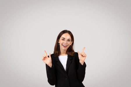 Foto de Mujer de negocios joven caucásica radiante con una amplia sonrisa apuntando hacia arriba con ambas manos, señalando un resultado positivo o dirigiendo la atención a la información útil arriba - Imagen libre de derechos