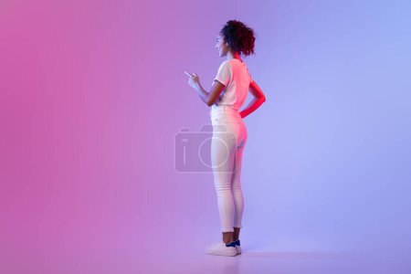 Foto de Mujer negra enfocada en blanco apuntando a una pantalla invisible, imitando la interacción con la pantalla táctil, colocada contra el fondo de degradado de rosa a azul, espacio libre - Imagen libre de derechos