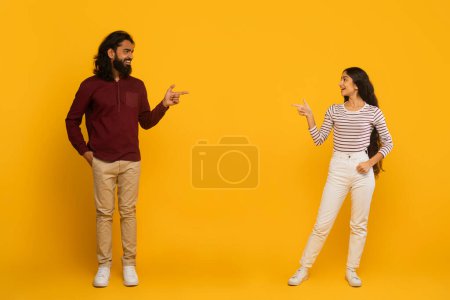Photo for Man and woman smiling and pointing at each other on a clean yellow background with friendly interaction - Royalty Free Image