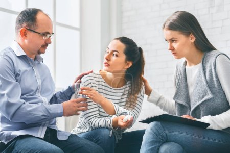 Photo for Concerned support group mebers comforting emotional young woman at therapy session, offering glass of water, panorama - Royalty Free Image