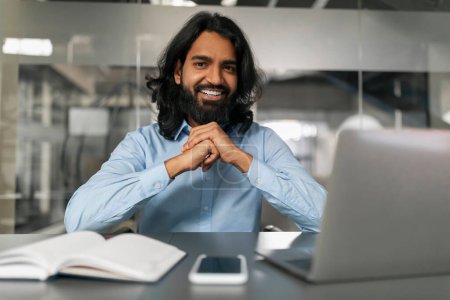 Confident, bearded professional smiles and poses for a portrait in a modern corporate office setting