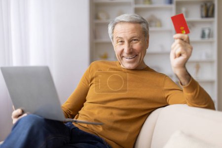 Photo for A grinning elderly man wields a credit card alongside his laptop, likely engaging in an online purchase or banking - Royalty Free Image