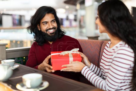 Photo for Beautiful loving young indian man and woman exchanging gifts at cafe, sitting at table, drinking coffee, enjoying time together. Date, anniversary celebration, relationships - Royalty Free Image