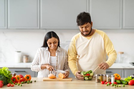 Photo for Joyful Indian Couple Cooking Food And Smiling Preparing Salad For Dinner Together In Kitchen At Home On Weekend. Eastern Husband And Wife Cook Meal. Healthy Nutrition And Family Recipes Concept - Royalty Free Image