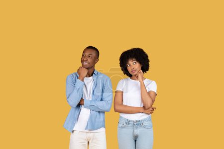 Photo for Two young African American individuals lean on their hands with thoughtful expressions, standing against a mustard yellow backdrop, contemplating a decision or idea, studio - Royalty Free Image