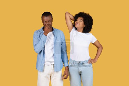 Photo for Sad millennial African American man chuckling with his hand over his mouth while the woman beside him looks up with her hand on her hip, both showing signs of relaxed amusement on a yellow backdrop - Royalty Free Image