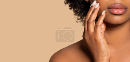 Close-up of black womans lips and delicate hand gesture, highlighted by her curly hair and flawless skin against beige background