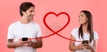 Téléchargez les photos : Un homme et une femme souriants en t-shirts blancs textent sur des smartphones, connectés par une boucle de coeur rouge sur un fond rose vif, symbolisant une connexion numérique aimante - en image libre de droit