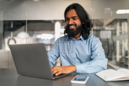 Téléchargez les photos : Homme professionnel détendu avec un sourire décontracté travaillant sur son ordinateur portable dans un cadre de bureau confortable - en image libre de droit