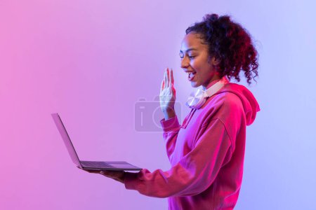 Téléchargez les photos : Personne dans un sweat à capuche rouge en utilisant des gestes de main pour interagir avec un ordinateur portable flottant dans un fond bicolore - en image libre de droit
