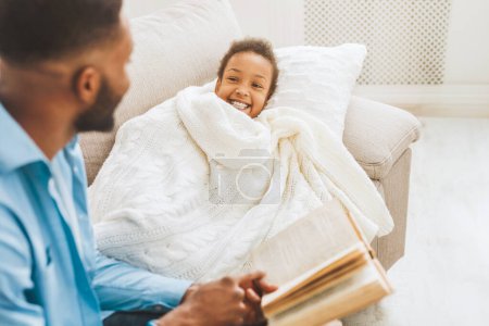 Téléchargez les photos : Père lisant conte de fées à la petite fille avant de dormir sur le canapé - en image libre de droit