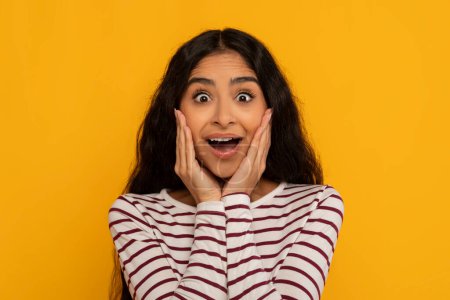 Téléchargez les photos : Une jeune femme excitée avec une expression surprise se dresse sur un fond jaune vif - en image libre de droit