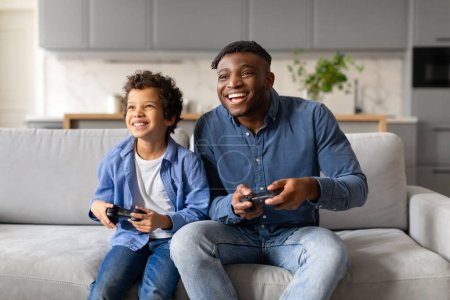 Foto de Un momento de alegría cuando un niño y su padre participan en una competición de videojuegos juguetones en el sofá - Imagen libre de derechos