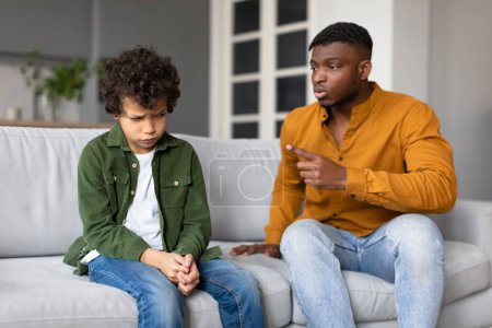 Un père semble parler sérieusement à son fils, l'enfant regarde en bas et le père pointe du doigt
