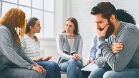 Psychotherapy, depression, life issues concept. Depressed man sitting at rehab group therapy and thinking about his problems