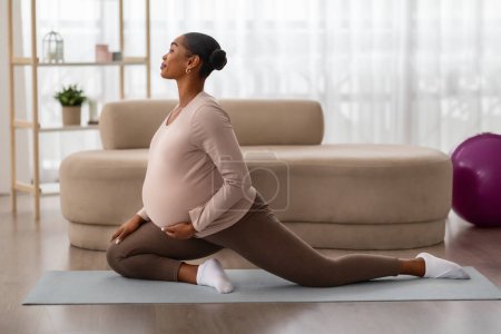Téléchargez les photos : Femme afro-américaine enceinte étirant les jambes s'entraînant à la maison. Femme noire enceinte fait échauffement exercice d'aérobic sur tapis de yoga, concept de grossesse saine, espace de copie - en image libre de droit