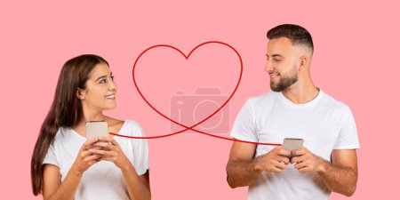 Photo for A woman and man, both in white t-shirts, are looking at each other with a smile while holding smartphones, connected by a red heart outline against a salmon pink background - Royalty Free Image