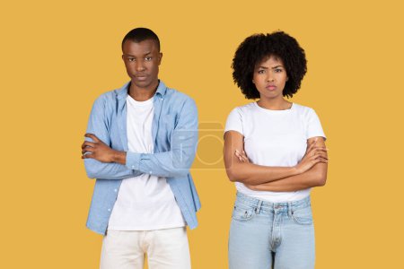 Téléchargez les photos : Jeune couple afro-américain en colère face à la caméra avec des expressions sérieuses et les bras croisés, représentant un moment de désaccord ou de détermination sur un fond jaune - en image libre de droit