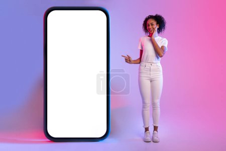 Foto de Mujer con una expresión agradable que presenta un teléfono inteligente maqueta gigante contra un fondo de degradado de color - Imagen libre de derechos