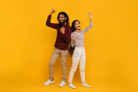 A man and woman both throw a fist in the air in excitement, set against a yellow backdrop