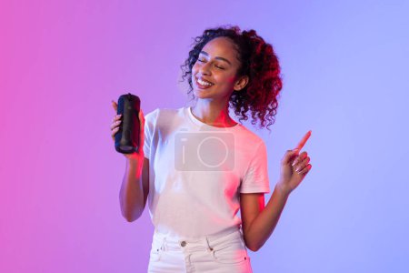 Una mujer alegre con el pelo rizado sostiene un controlador de juego y la pluma con una luz de fondo de color