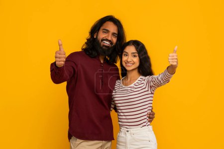 Foto de La pareja apoya alegremente con pulgares hacia arriba y sonrisas radiantes, lo que sugiere positividad y alegría en un entorno amarillo - Imagen libre de derechos