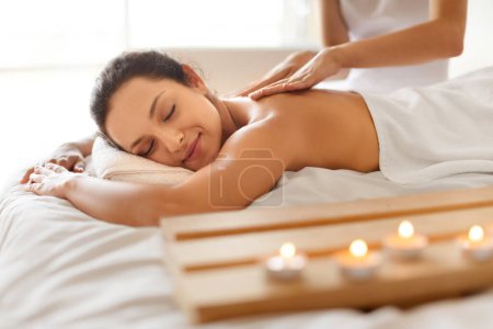 Téléchargez les photos : Femme paisible lors d'une séance de massage couchée bénéficiant d'un traitement de beauté à l'intérieur, recevant un mélange professionnel de relaxation et de rajeunissement du corps au salon de beauté. Concept de spa et bien-être - en image libre de droit